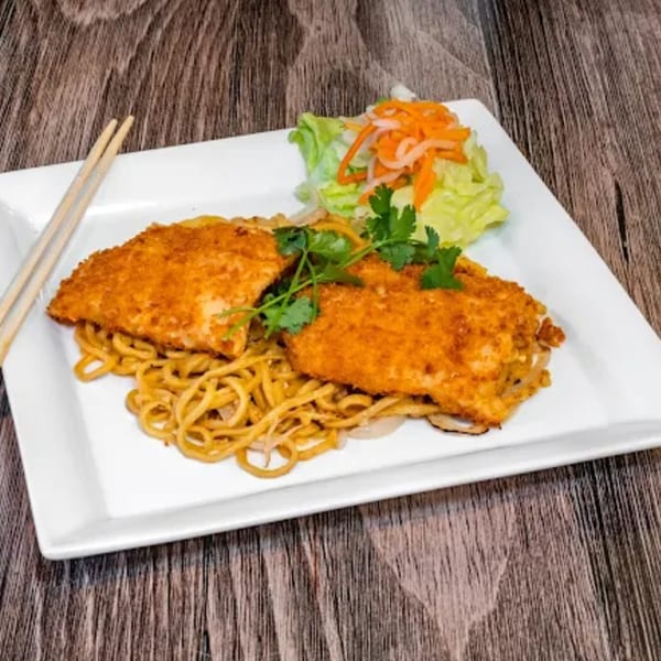 Crispy chicken over noodles with a side salad and chopsticks on a white rectangular plate.