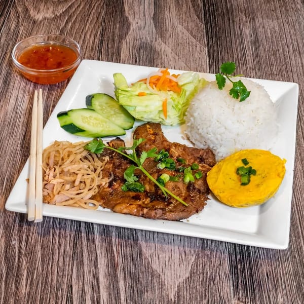 Vietnamese grilled pork chop with rice, egg cake, salad, and sweet chili sauce.