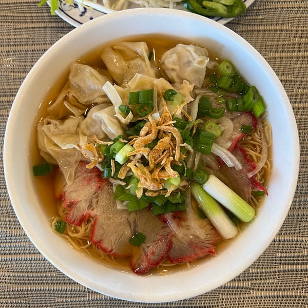 A bowl of Vietnamese wonton noodle soup with char siu pork, green onions, and fried shallots.