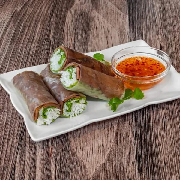 Four fresh Vietnamese spring rolls with rice, lettuce, and meat, served with a side of chili sauce.