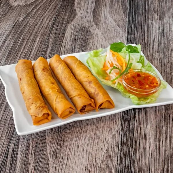 Four crispy Vietnamese spring rolls with lettuce, pickled vegetables, and a dipping sauce.