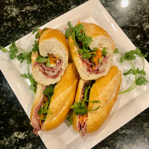 Four Vietnamese banh mi sandwiches, filled with meat, pickled vegetables, and cilantro, on a white platter.