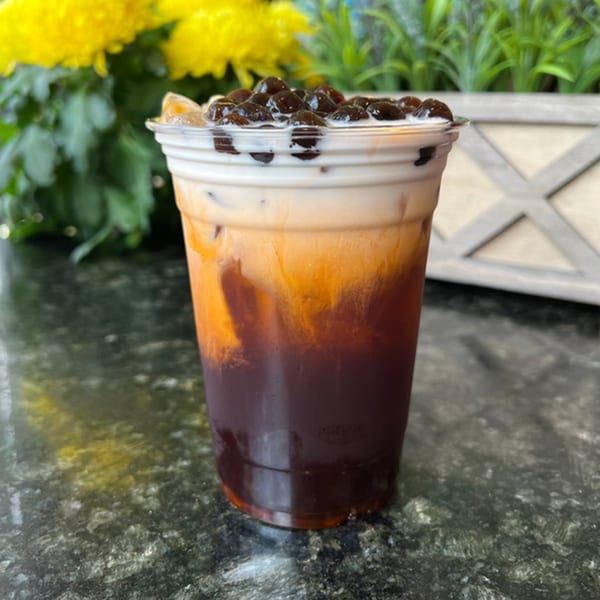 Vietnamese iced coffee with boba pearls and cream, on a dark counter with yellow flowers.