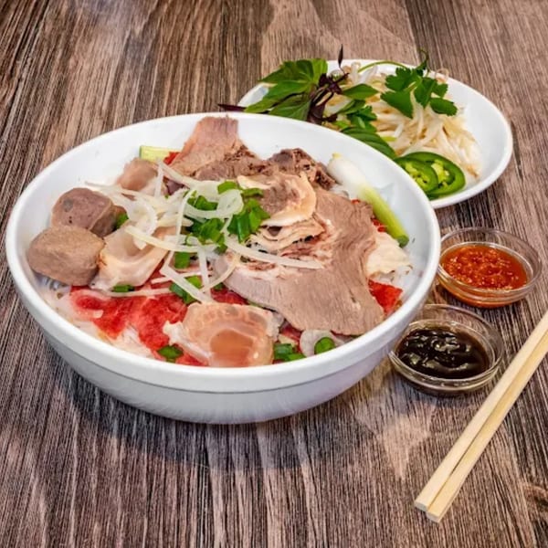 A bowl of Pho Dublin's Vietnamese pho with various meats, herbs, and sauces on a wooden table.