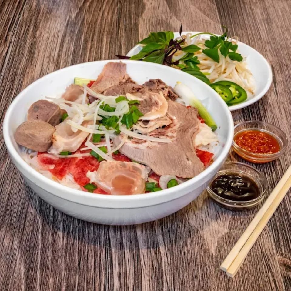 A bowl of Pho Dublin's Vietnamese pho with various meats, herbs, and sauces on a wooden table.